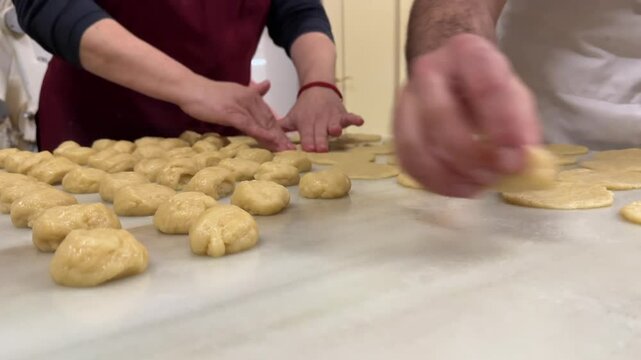A close up view of the hands of two pastry chef preparing handmade traditional Spanish sweet potato fritters on a white color marble table in a traditional workshop. 4K
