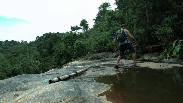 A tourist walks along the cliff of a mountain waterfall in the jungle