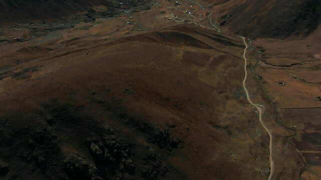 Drone reveal shot transitioning from top-down view over scenic mountain road to stunning valleys and remote village. Chaullaocha and Chupani communities in Peru, Cusco, Lares Trek