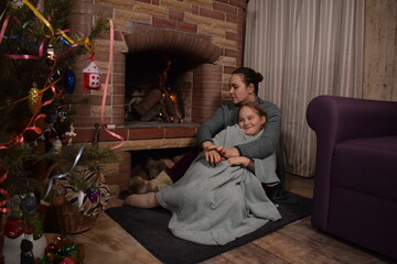 A young parent and child enjoy cozy leisure time by the fireplace, embracing the warmth and comfort of winter time indoors. Hygge concept. Family bonds and shares precious moments together t home