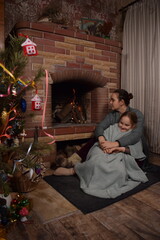 A young parent and child enjoy cozy leisure time by the fireplace, embracing the warmth and comfort of winter time indoors. Hygge concept. Family bonds and shares precious moments together t home