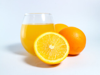 Fresh orange juice in a glass with whole and sliced oranges on a white background