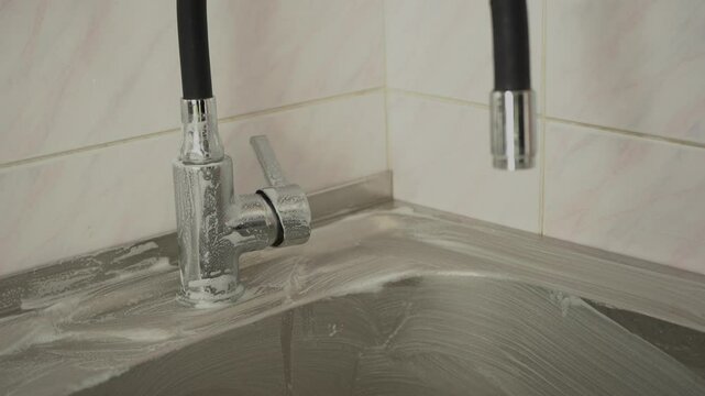 Cleaning kitchen sink of stainless steel with foamed detergent product and brawn sponge. Scrubbing the dirt.