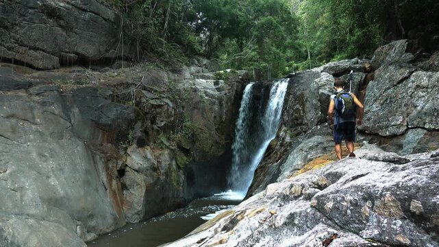 A tourist climbs over rocks to a waterfall in the jungle