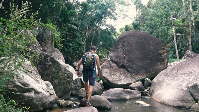 A tourist walks inside a streambed over rocks to a huge boulder