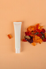 Plastic white tube for cream or lotion. Skin care or sunscreen cosmetic with stylish props and fruit gummi on cream background.