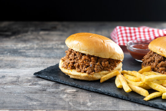 Traditional sloppy joe sandwich with french fries on wooden table and black background. Copy space