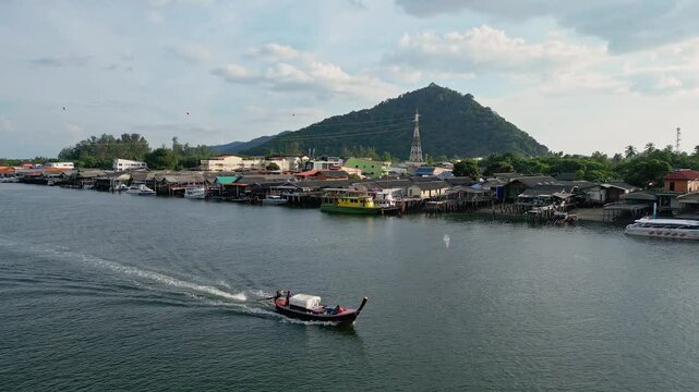 Koh Lanta, Thailand: Aerial backward drone footage of a long tail boat sailing along the the Sala Dan town in Koh Lanta island in the Andaman sea in southern Thailand. 