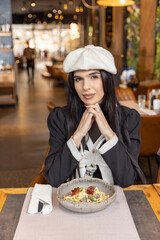 Beautiful young woman with a hat posing at a table in a restaurant