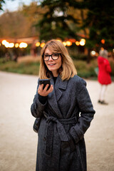 Fototapeta premium Attractive mid aged woman walking on the street and using her smartphone