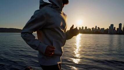 Silhouette of a person jogging by the water at sunset, captured from a side angle. The video evokes a serene, motivational vibe with urban skyline in view.
