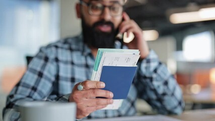 Bearded man in modern office holding passport and flight tickets while on phone call confirming last travel details.