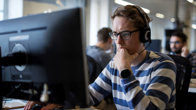 Focused worker wearing headphones on computer in busy office