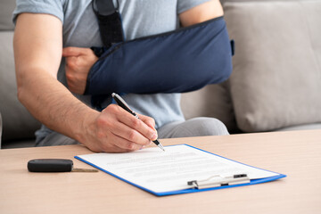 Close up of a man hands with broken arm signing insurance document after car accident at home