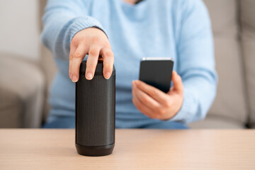 Close-up on female hand using phone connecting speaker bluetooth at home.