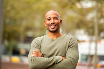 confident man with arms crossed outdoors, smiling at the camera