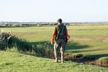 Mature hunter man holding a shotgun and walking through a field