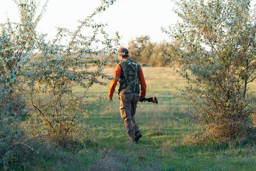 Mature hunter man holding a shotgun and walking through a field