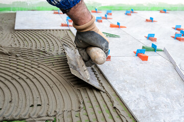 Bricklayer tiler spreads cement glue with notched trowel to install tiles for a new floor....
