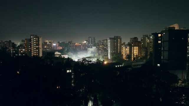 Aerial drone shot over Mumbai city at night, revealing a wedding venue with bright lights, trees, and tall buildings. Stunning urban view with glowing streets and illuminated skyline