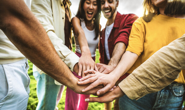 Multiracial group of young people stacking hands outdoors - Happy friends celebrating success on city street - Youth community concept with guys and girls standing together supporting peace and love