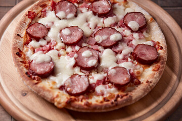 Pizza with sausage, ham and mozzarella cheese on wooden background. Soft focus. Close up