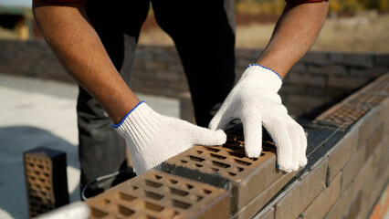 Construction worker carefully laying bricks on fresh cement, using precise hammer and level techniques while building sturdy wall section with professional masonry skills