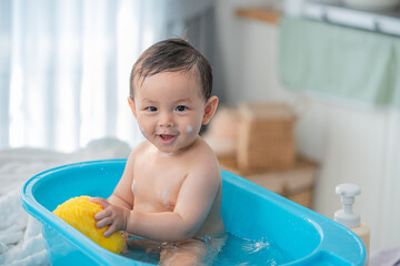 Baby enjoying a bath in a blue tub with a yellow sponge in a bright, cozy bathroom