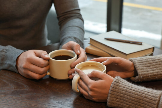 Colleagues having coffee break at wooden table in cafe, closeup