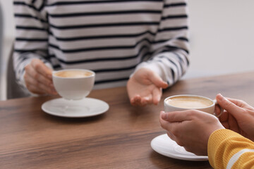 Coffee break. Women with cups of hot drinks at wooden table indoors, closeup