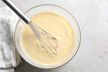 Whisk and bowl of dough on grey table, top view
