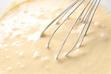 Whisk and bowl of dough, closeup view