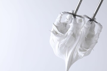 Whisks with whipped cream on white background, closeup. Space for text