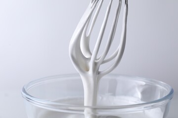 Whisk and bowl with whipped cream on white background, closeup