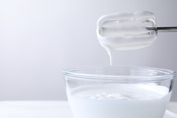 Hand mixer with whisks and bowl of whipped cream on white table, closeup. Space for text