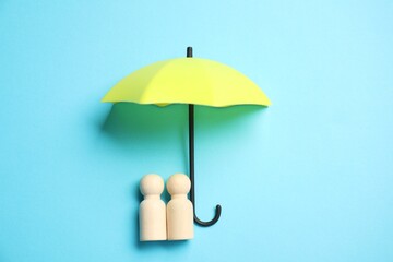 Human figures under umbrella on light blue background, top view. Insurance concept