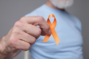 Multiple Sclerosis awareness. Senior man with orange ribbon on grey background, closeup