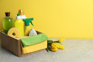 Spring cleaning. Detergents, supplies and tulips on light grey table against yellow background,...