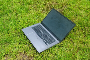 A laptop with a black screen and grey keyboard is placed on green grass outdoors. This image is ideal for themes related to remote work, outdoor computing, or digital nomad lifestyle