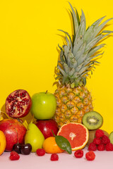 Vertical image of colorful tropical fruits on a yellow background with pink,pineapple,banana,kiwi,grapes,peach,pear,apple,raspberry,cherry,pomegranate,tangerines,grapefruit. healthy food