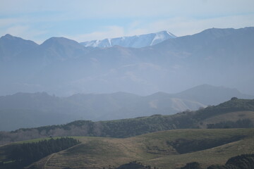 A panoramic view of a mountain range in New Zealand with clear skies and soft sunlight. A stunning scene showcasing the beauty of untouched wilderness.
