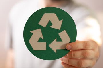 Close-up of a hand holding a green circular recycle symbol. Eco-friendly concept.