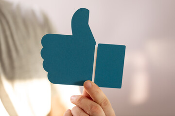 Hand holding a teal paper thumbs up. Positive feedback, approval, like concept.