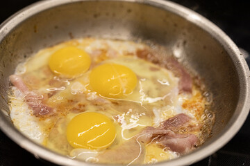 Close-up of three fried eggs cooking in a pan with bacon. Delicious breakfast food.