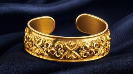 A luxury gold cuff bracelet with an intricate carved pattern displayed on a dark fabric