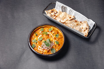 indian food on a gray background,served on a black plate,with pita bread on the side
