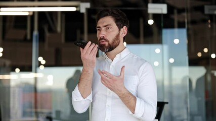 Successful businessman talking on smartphone using speakerphone in modern glass office. Bearded man in white shirt using mobile phone.