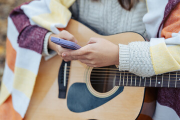 Closeup of woman hands with a phone and guitar. Young girl playing the guitar, took a break to...