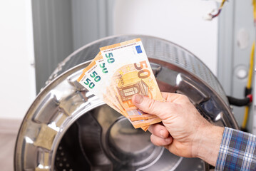 Man hand with euro bills pays for service of washing machine. High price for repair and maintenance of washer