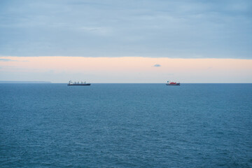 Two cargo ships on the horizon of the Atlantic Ocean, Portugal. Calm sea, cloudy sky with a glimpse of sunset.
